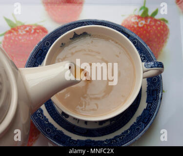 English tea time : Verser du thé Earl Grey tea pot de bleu et blanc dans une tasse de thé sur les fraisiers Banque D'Images