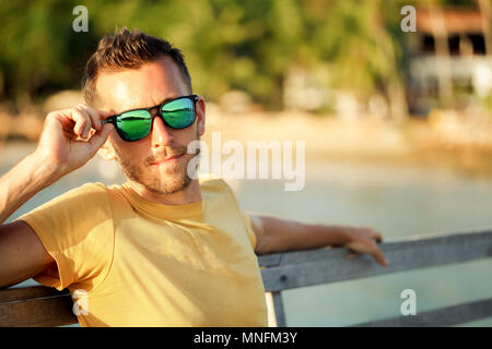 Été Voyage Vacances. Bel Homme à lunettes Lunettes de soleil à la mode de plage tropicale avec décor fond flou Banque D'Images