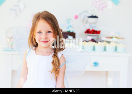 Adorable petite fée fille avec les ailes sur une fête près de la table à dessert Banque D'Images