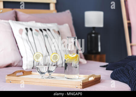 Bouteille et deux verres avec de l'eau citronnée debout sur plateau en bois sur le lit Banque D'Images