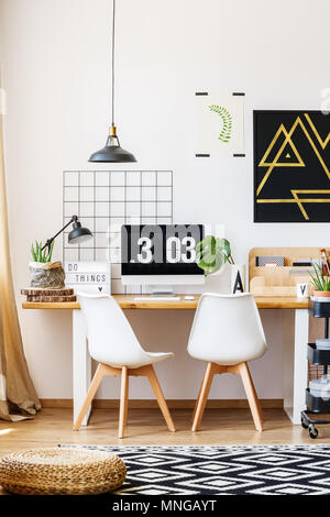 Deux blanches des chaises de créateur et un bureau en bois dans une salle au décor contemporain, monstera plante, poster, Ordinateur et accessoires hippie Banque D'Images