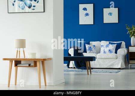 Table en bois et blanc canapé dans salon élégant avec des affiches de fleurs Banque D'Images