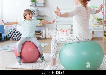Physiothérapeute et jeune garçon faisant exercice s'étendant sur les boules colorées dans cette chambre lumineuse Banque D'Images