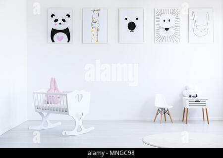 Oreiller rose en blanc berceau en chambre de bébé avec petite chaise et armoire contre le mur avec une galerie d'affiches d'animaux Banque D'Images