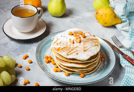 Petit-déjeuner fait maison : american style crêpes servies avec du sucre des baies et powderwith une tasse de thé sur fond de béton. Banque D'Images