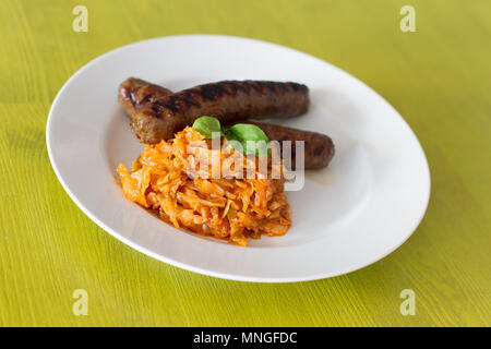 Saucisses grillées avec pose de chou dans une assiette blanche, sur une table jaune Banque D'Images