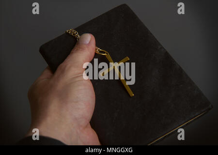 Une main d'homme est titulaire d'une bible dans un classeur noir une croix de métal sur une chaîne close-up Banque D'Images