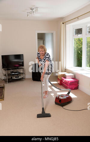 Déménagement, femme à l'aide d'un aspirateur pour aspirateur très hoover le tapis et faire des exercices stretch jambe Banque D'Images