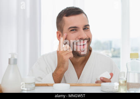 Bel homme joyeux de mettre de la crème sur son visage Banque D'Images