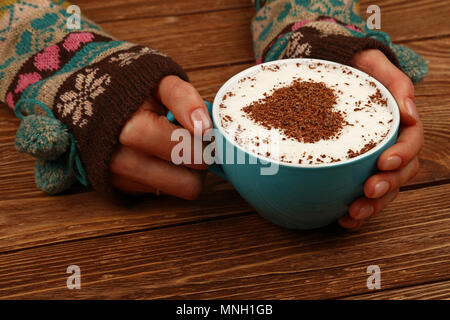 Close up femme deux mains tiennent et Big hug pleine tasse de Cappuccino, Latte avec coeur en chocolat sur mousse de lait sur la table en bois brun, haut Banque D'Images