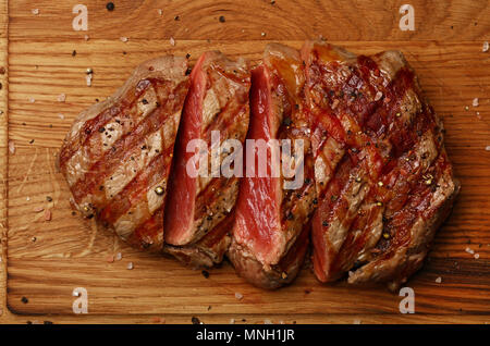 Près d'un rosé rôti grillé Ribeye Steak de boeuf en tranches sur une planche à découper en bois, vue d'en haut, juste au-dessus Banque D'Images