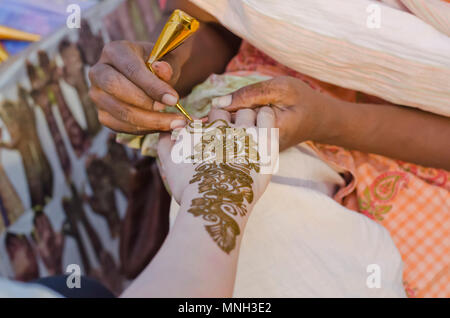 Un artiste à l'henné Shilparamam arts and crafts village, Hyderabad, Inde, l'application de pâte mehndi sur le côté d'une touriste. Art & la diversité. Banque D'Images