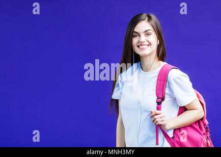 Portrait of beautiful smiling fille brune vêtue de blanc T-shirt rose avec sac à dos et casque avant fond violet Banque D'Images