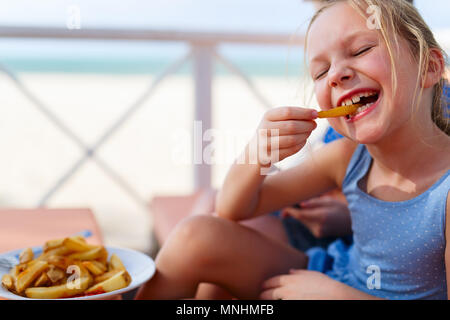 Adorable petite fille avoir une saine alimentation frites au restaurant en plein air sur la journée d'été Banque D'Images