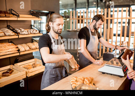 Deux belles ventes en uniforme Vente de pain à une jeune femme debout à la clientèle au comptoir de la boulangerie Banque D'Images