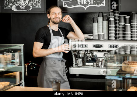 Portrait of a handsome barista en uniforme, debout près de la machine à café au café Banque D'Images