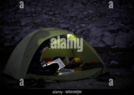 Backpackers d'oeil sur la carte par projecteur dans leur tente au camp au lac de l'ours brun sur un trek de deux semaines de la Haute Route dans la Sierra John Muir Wilderness en Californie. La route de 200 milles environ en parallèle avec le John Muir Trail populaire à travers la Sierra Nevada de Californie Plage de Kings Canyon National Park Le Parc National de Yosemite. Banque D'Images