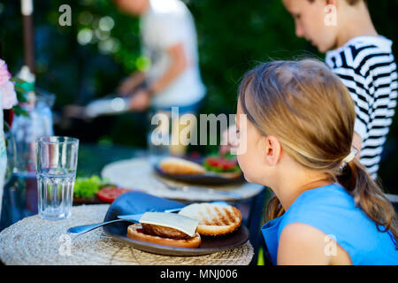 Adorable petite fille et sa famille manger de délicieux hamburgers faits maison à l'extérieur sur journée d'été Banque D'Images