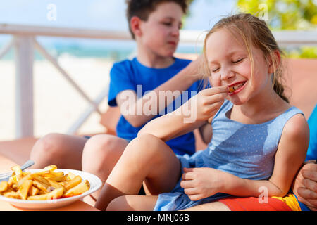 Adorable petite fille profiter de manger des frites avec son frère à l'extérieur restaurant sur journée d'été Banque D'Images