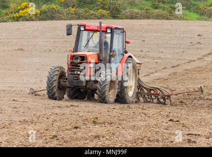 Agriculteur en Irlande l'ensemencement une récolte de blé avec un semoir tête remorqué par un tracteur. Banque D'Images