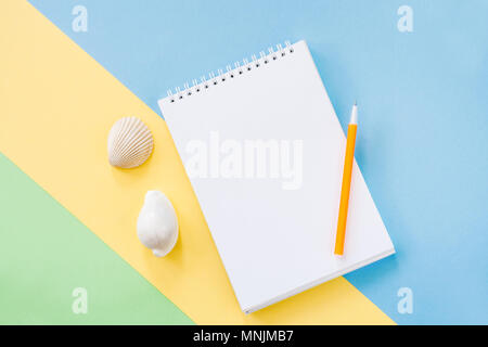 Vacances d'été concept avec une bande jaune, blanc bloc-notes, stylo orange et deux coquillages sur fond bleu-vert. Banque D'Images