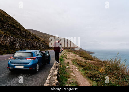 Femme se dresse sur la clôture en pierres en scenic route irlandaise. Elle est le moteur de la voiture de location Banque D'Images