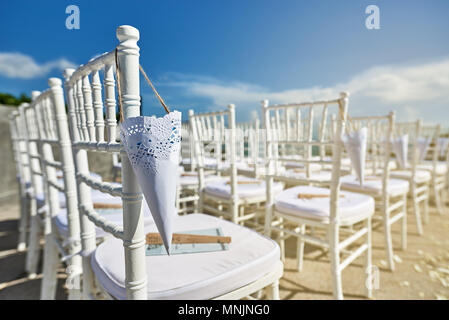 Salle de mariage plage configuration avec style moderne de chaises chiavari blanche avec cône de pétale de rose et le coucher de la lumière direct du côté droit Banque D'Images