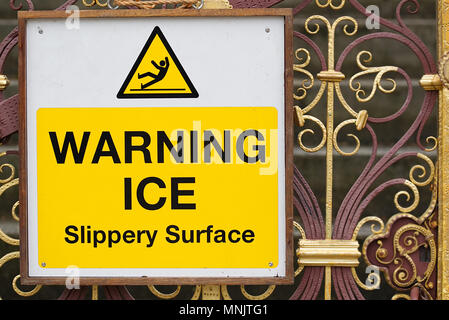 Glace avertissement surface glissante signer le texte noir sur fond blanc et jaune avec symbole d'un homme de glisser sur la glace sur des portes de fer. Le gel hivernal Banque D'Images