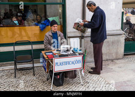 Un homme lit un journal à côté d'un homme offrant un service de laminage à Lisbonne, Portugal. Banque D'Images