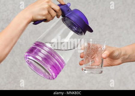 Mains verser de l'eau d'une cruche dans un verre d'une autre personne Banque D'Images