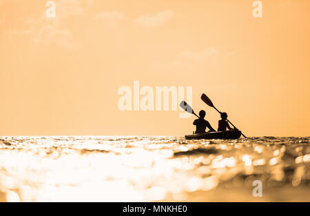 Silhouettes famille de mère et fille à la pagaie en kayak au coucher du soleil de l'océan tropical Banque D'Images