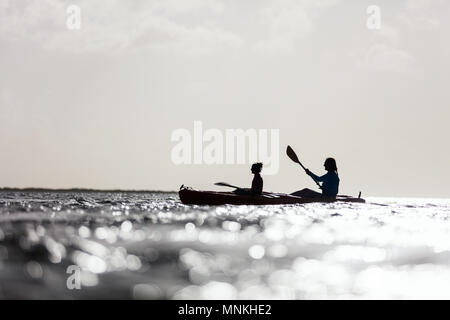 Silhouettes famille de mère et fille à la pagaie en kayak au coucher du soleil de l'océan tropical Banque D'Images