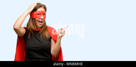 L'âge moyen super hero woman wearing red Cape et masque l'opposé côté avec fond bleu isolé de doigt Banque D'Images