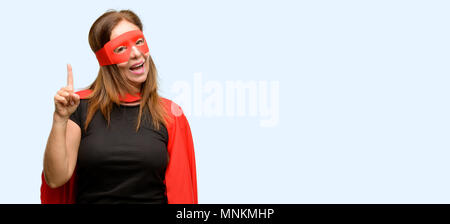 L'âge moyen super hero woman wearing red Cape et masque l'opposé côté avec fond bleu isolé de doigt Banque D'Images