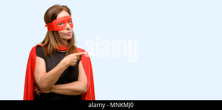 L'âge moyen super hero woman wearing red Cape et masque l'opposé côté avec fond bleu isolé de doigt Banque D'Images