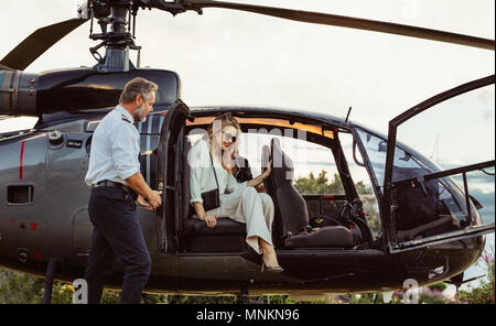 Belle jeune femme sortir d'un hélicoptère avec pilote masculin par permanent. Femme voyageant par son hélicoptère. Banque D'Images