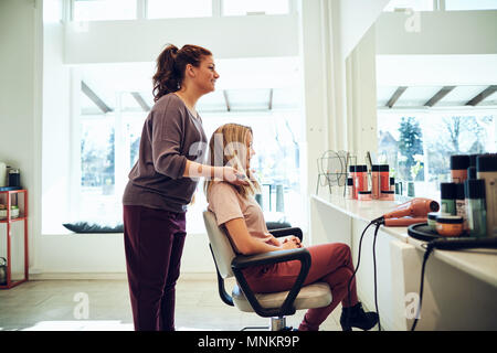 Smiling young coiffure styling finition les cheveux d'un client femme assise sur une chaise tout en travaillant dans son salon Banque D'Images