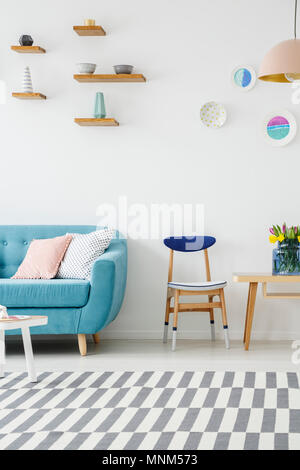 Photo recadrée d'un canapé, table, chaise en bois, tapis à rayures et des étagères avec décoration sur le mur dans un salon intérieur Banque D'Images