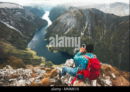 Man using smartphone backpacker détente sur sommet de montagne qui voyage seul en Norvège vie aventure vacances actives La technologie moderne de la génération Y Banque D'Images