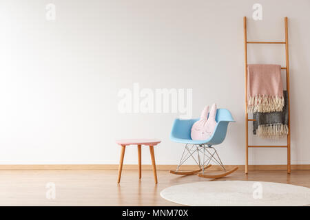 Copie espace de mur vide en simple chambre d'enfant avec des couvertures sur l'échelle, un oreiller sur bleu rocking chair, tapis et selles Banque D'Images