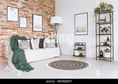 Couverture vert sur blanc canapé et les oreillers dans la salle de séjour avec des tapis, lampe et affiches simples Banque D'Images