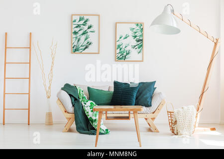 Échelle en bois et des branches dans vase décoratif à côté de canapé avec une couverture et des oreillers floral vert Banque D'Images