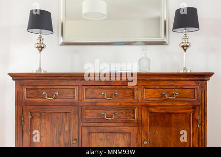 Commode en bois élégant, deux petites lampes et un miroir dans un cadre moderne Banque D'Images