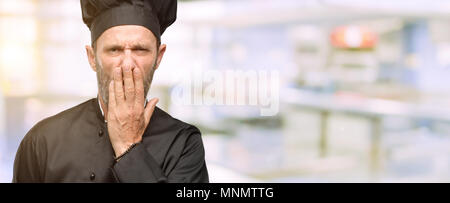 Cuisinier en chef, l'homme portant hat couvrir la bouche sous le choc, l'air timide, l'expression de silence et d'erreur concepts, peur à une cuisine de restaurant Banque D'Images