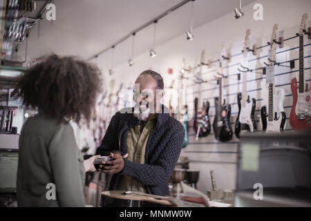 Senior male payer dans un magasin de guitare avec carte de crédit Banque D'Images