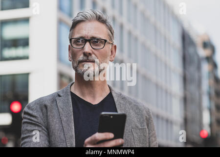 Homme mature et marche sur sur smartphone en ville Banque D'Images