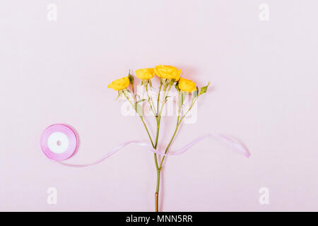 Petit ruban de satin avec des roses jaunes sur fond rose pale, vue du dessus. Composition minimale de mise à plat avec l'exemplaire de l'espace. Banque D'Images