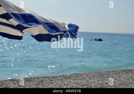 Un bleu-et-blanc-bar d'un parasol sur la plage rocheuse waterfront à Nice, France Banque D'Images