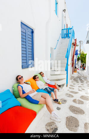 Mère de famille et deux enfants se détendre sur un des oreillers colorés au café en plein air sur la rue de village grec traditionnel Banque D'Images