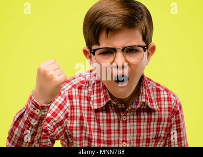 Beau tout-petit enfant aux yeux verts irrité et en colère exprimer une émotion négative, ennuyé par quelqu'un sur fond jaune Banque D'Images